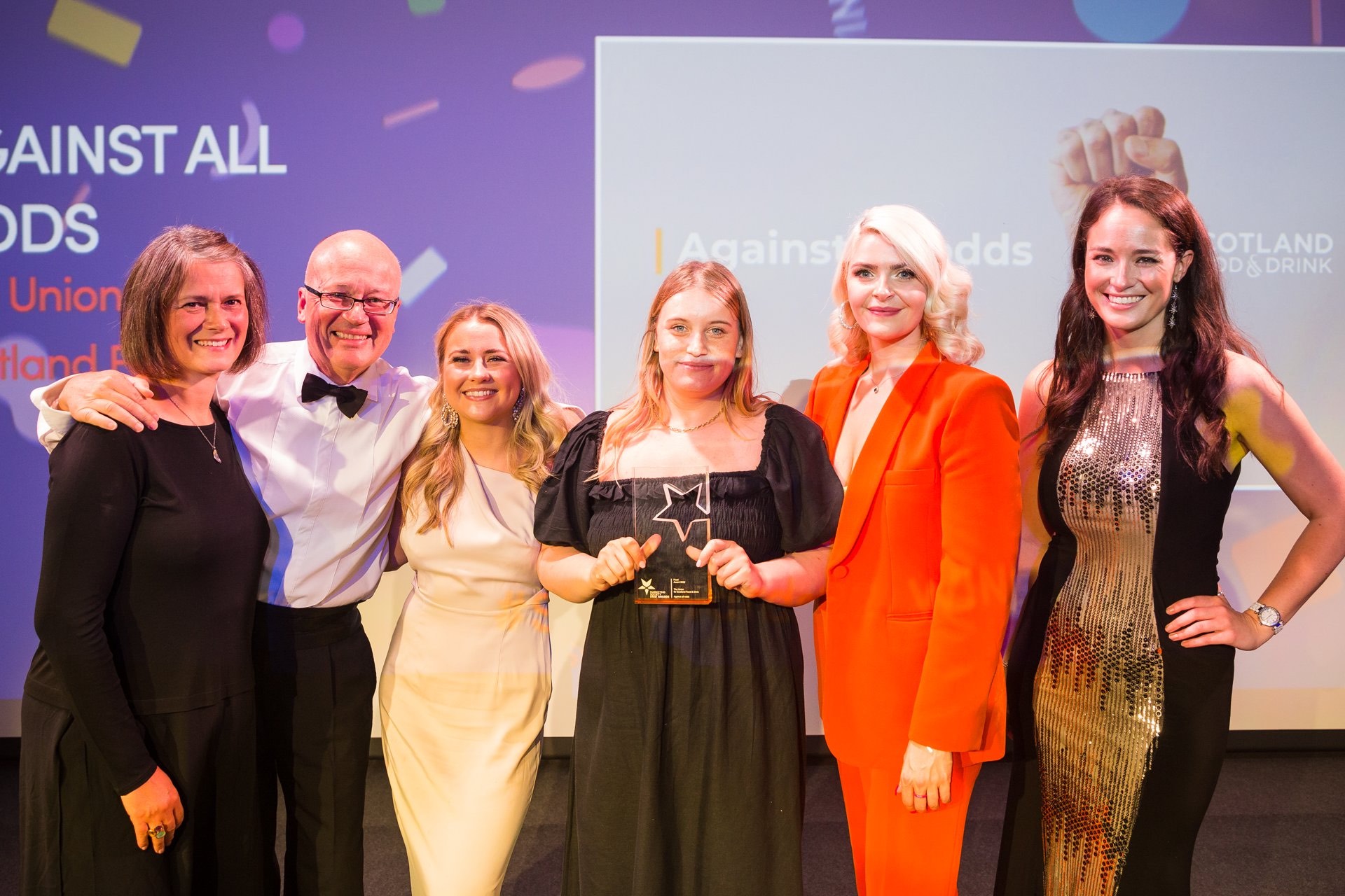 5 ladies and one man standing facing to camera holding award statue