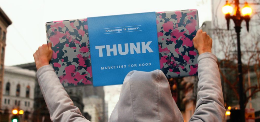 Person in grey hoodie holding up banner for Thunk