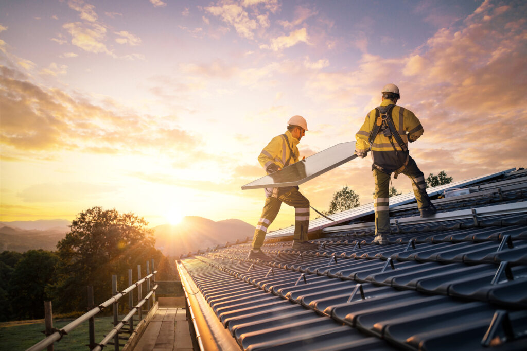Workmen adding solar panels to roof at sunset